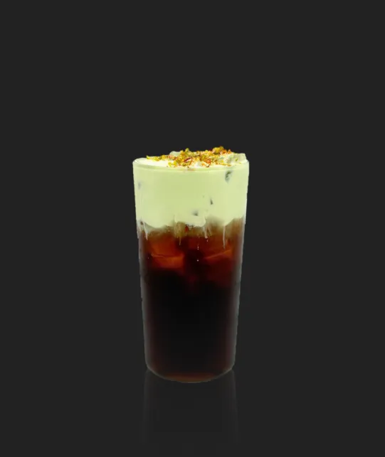 Tall glass of iced coffee with dark espresso at the bottom, creamy foam on top, and crushed nuts on a dark background.