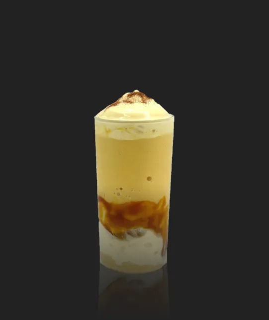Tall glass of layered caramel coffee drink topped with whipped cream against a dark background.