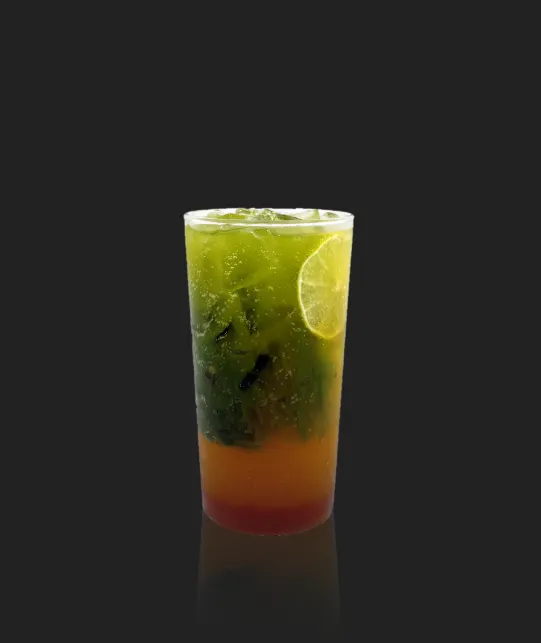 Layered tropical cocktail with lime wedge garnish on the rim and mint leaves, transitioning from green at the top to orange and red at the bottom on a dark background.