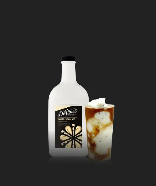 Bottle of DaVinci Gourmet White Chocolate sauce beside a tall glass of iced coffee topped with whipped cream