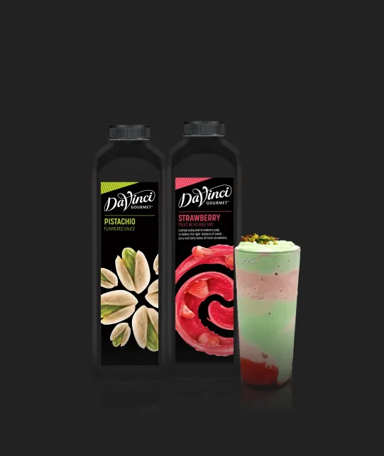 Two DaVinci Gourmet syrup bottles (pistachio and strawberry) with a layered green-pink beverage beside them on a dark background, suggesting a dessert drink.