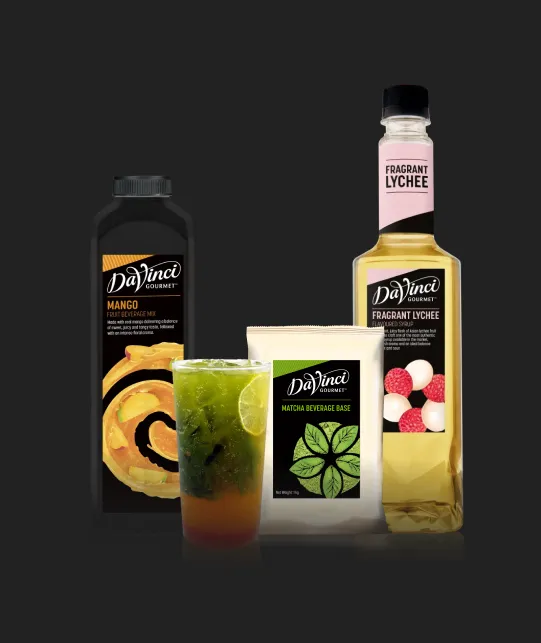 DaVinci Gourmet mango drink mix, fragrant lychee syrup bottle, matcha beverage base, and a glass of green iced drink on a dark background.