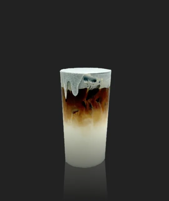 Layered iced coffee in a tall glass with white milk at the bottom, brown coffee in the middle, and a foamy top, against a dark background